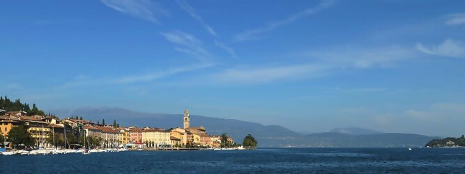 Trip Holiday beliebte Urlaubsziele am Gardasee -  Mit einer Fläche von 370 km² ist der Gardasee der größte See Italiens. Es liegt am Fuße der Alpen und erstreckt sich über drei Staaten: Lombardei, Venetien und Trentino. Die maximale Tiefe des Sees beträgt 346 m, er hat eine längliche Form und sein nördliches Ende ist sehr schmal. Dort ist der See von den Bergen der Gruppo di Baldo umgeben. Du trittst aus deinem gemütlichen Hotelzimmer und es begrüßt dich die warme italienische Sonne. Du blickst auf den atemberaubenden Gardasee, der in zahlreichen Blautönen schimmert - von tiefem Dunkelblau bis zu funkelndem Türkis. Majestätische Berge umgeben dich, während die Brise sanft deine Haut streichelt und der Duft von blühenden Zitronenbäumen deine Nase kitzelt. Du schlenderst die malerischen, engen Gassen entlang, vorbei an farbenfrohen, blumengeschmückten Häusern. Vereinzelt unterbricht das fröhliche Lachen der Einheimischen die friedvolle Stille. Du fühlst dich wie in einem Traum, der nicht enden will. Jeder Schritt führt dich zu neuen Entdeckungen und Abenteuern. Du probierst die köstliche italienische Küche mit ihren frischen Zutaten und verführerischen Aromen. Die Sonne geht langsam unter und taucht den Himmel in ein leuchtendes Orange-rot - ein spektakulärer Anblick.